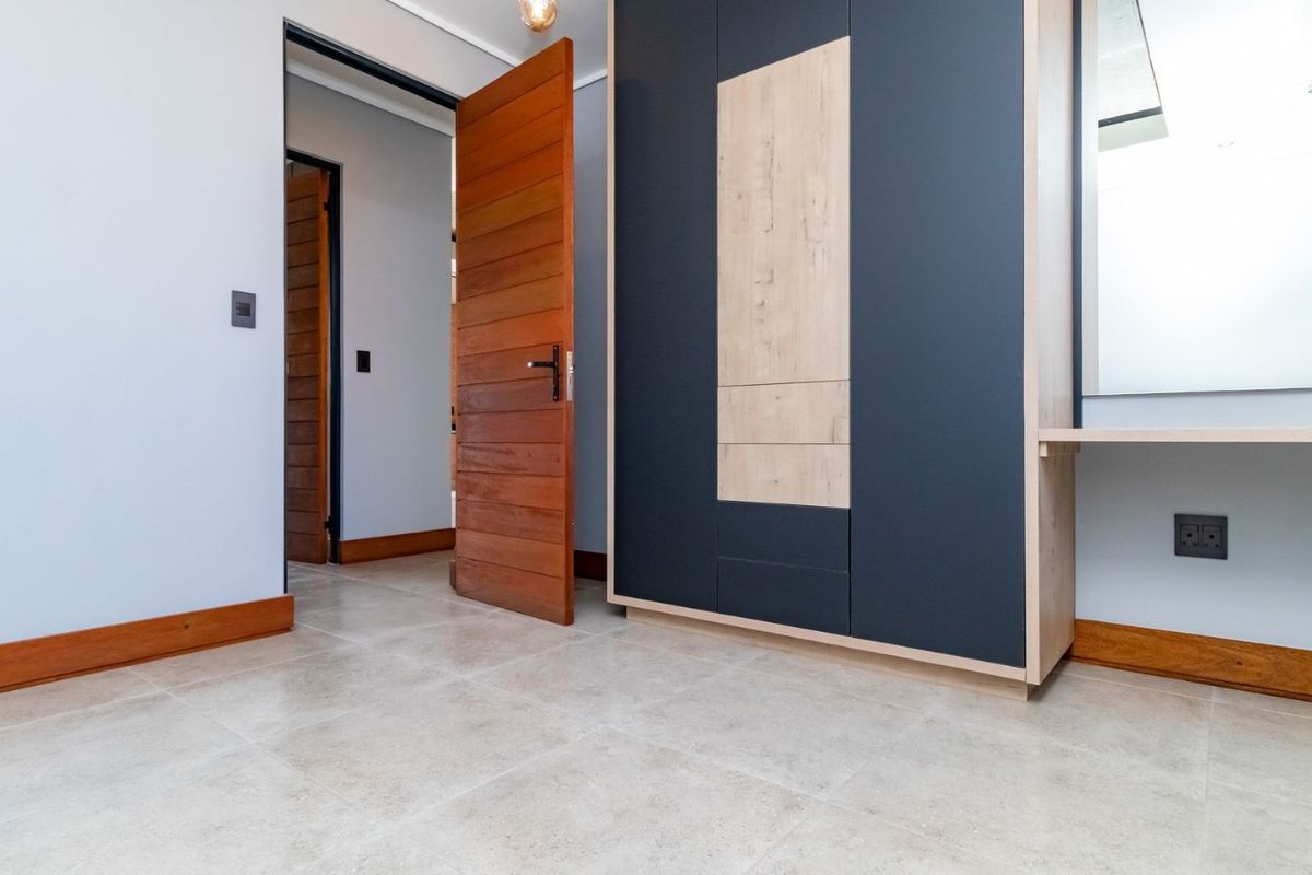 A clean, modern bedroom featuring neutral tiled flooring, a contemporary two-tone built-in wardrobe, and solid timber doors.