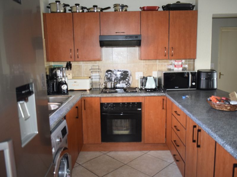 A functional kitchen featuring wood-finish cabinetry, laminate countertops, built-in oven with hob, extractor fan, and tiled flooring.