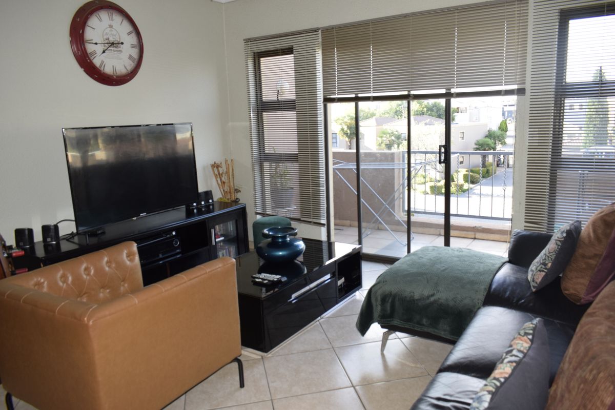 A living room featuring tiled flooring and a sliding glass door leading to a balcony, providing natural light through venetian blinds.