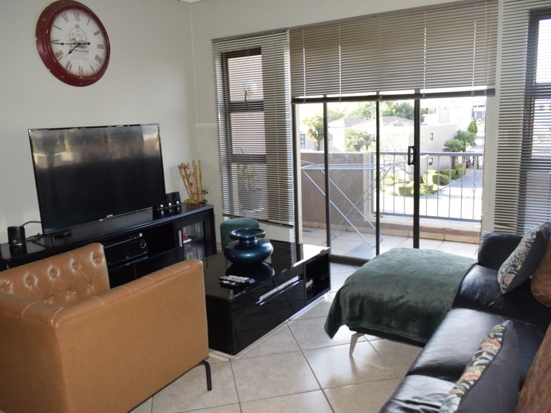 A living room featuring tiled flooring and a sliding glass door leading to a balcony, providing natural light through venetian blinds.