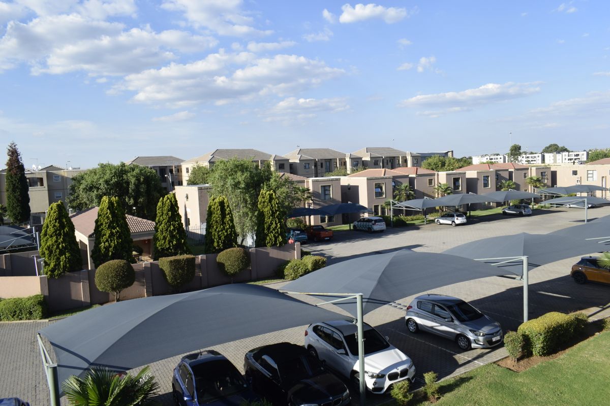 An elevated view of the townhouse complex featuring paved parking areas with shade cloth carports and well-maintained communal garden spaces.
