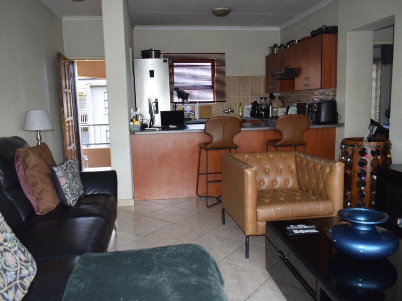 Open-plan living area featuring a functional kitchen with breakfast bar, tiled flooring, and direct access to an outdoor balcony.