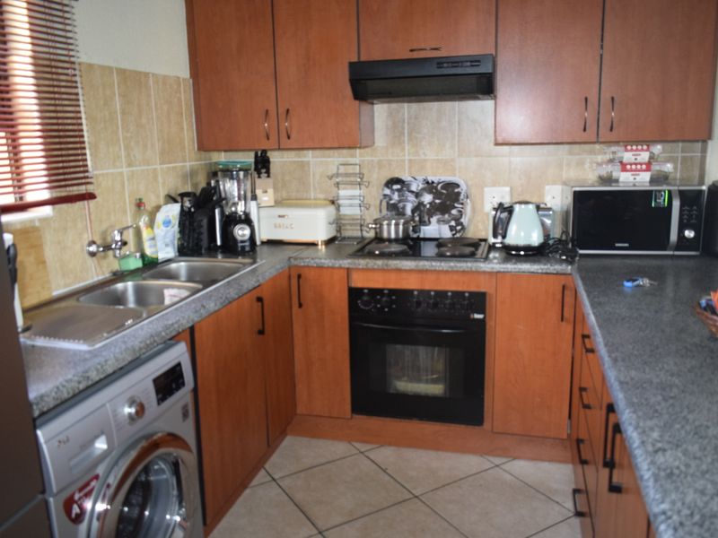 Functional kitchen featuring wood-finish cabinetry, granite countertops, built-in oven with hob, extractor fan, and dedicated space for a washing machine.
