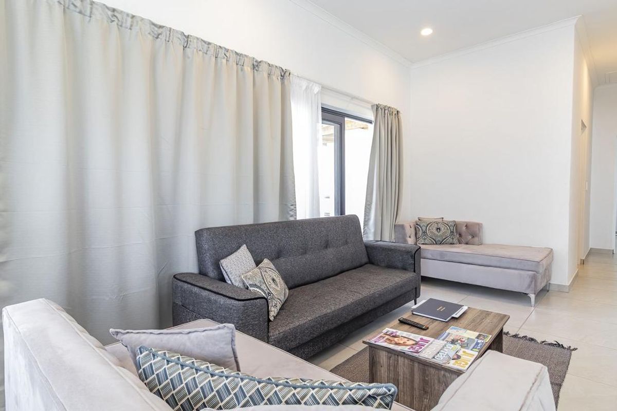 A bright and spacious living room featuring neutral tiled flooring, recessed downlighting, and large sliding glass doors leading to an outdoor area.