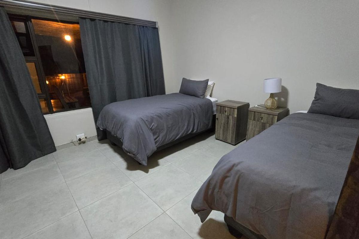 A bedroom featuring tiled flooring and large windows with curtains, providing a functional and neutral space.