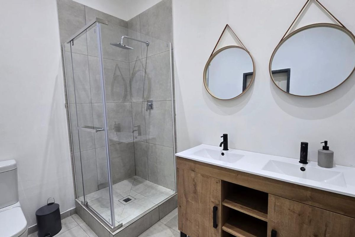 Modern bathroom featuring a glass-enclosed shower with grey tiling and a double vanity unit with integrated sinks and contemporary matte black fixtures.