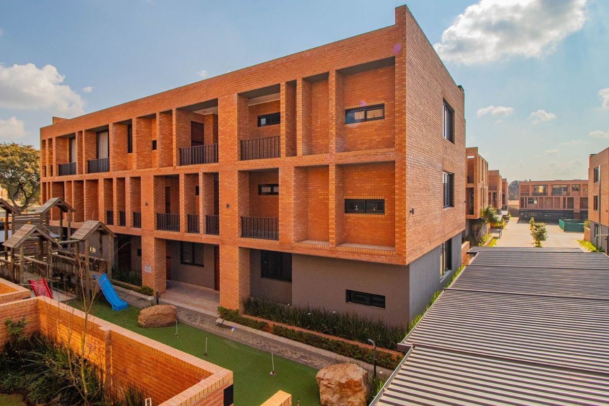 Modern multi-story apartment complex featuring exposed brick architecture, private balconies, and a well-maintained communal courtyard area with paved pathways.