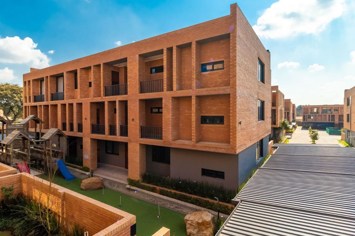 Aerial view of a modern multi-story apartment complex featuring exposed brick architecture, private balconies, and landscaped communal outdoor areas.