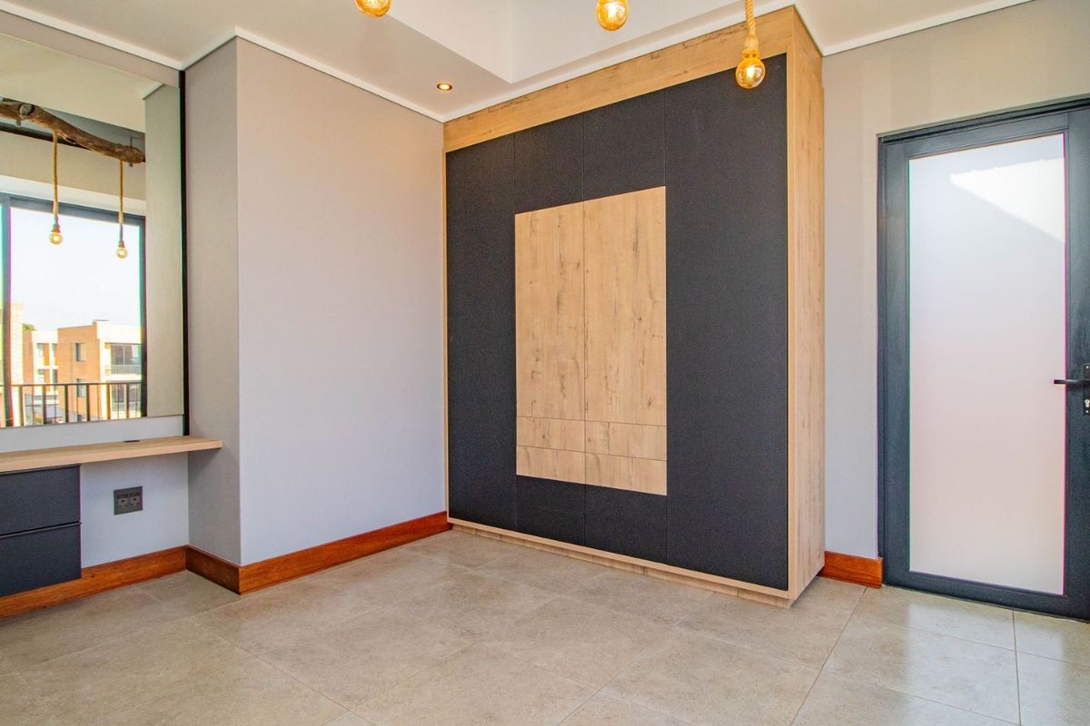 Modern bedroom featuring a large built-in wardrobe with contrasting wood and dark finishes, a built-in vanity, tiled floors, and a frosted glass door.