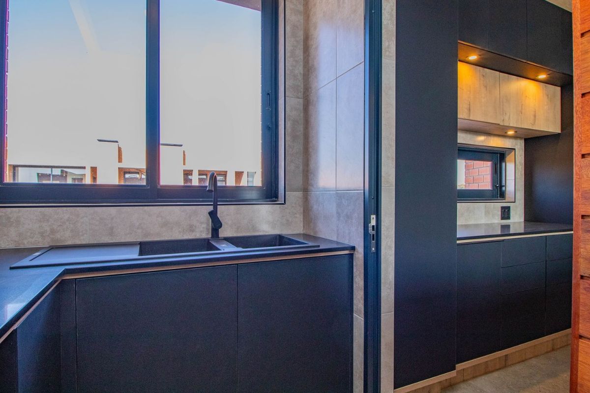 Modern kitchen featuring sleek dark cabinetry, stone countertops, a double sink with a matte black mixer tap, and integrated recessed lighting.