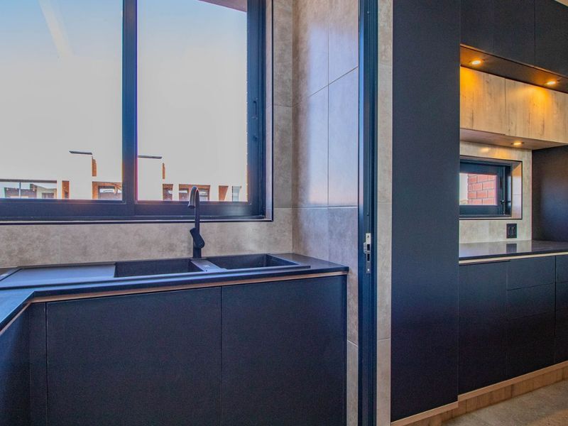 Modern kitchen featuring sleek dark cabinetry, stone countertops, a double sink with a matte black mixer tap, and integrated recessed lighting.