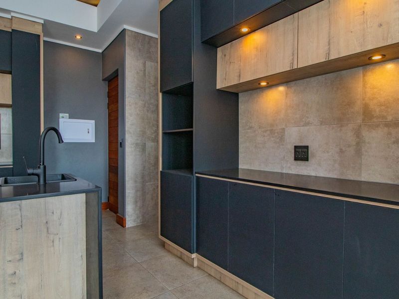 Modern kitchen featuring dark cabinetry, wood-tone accents, stone countertops, integrated lighting, and high-quality tiled finishes in a contemporary penthouse setting.
