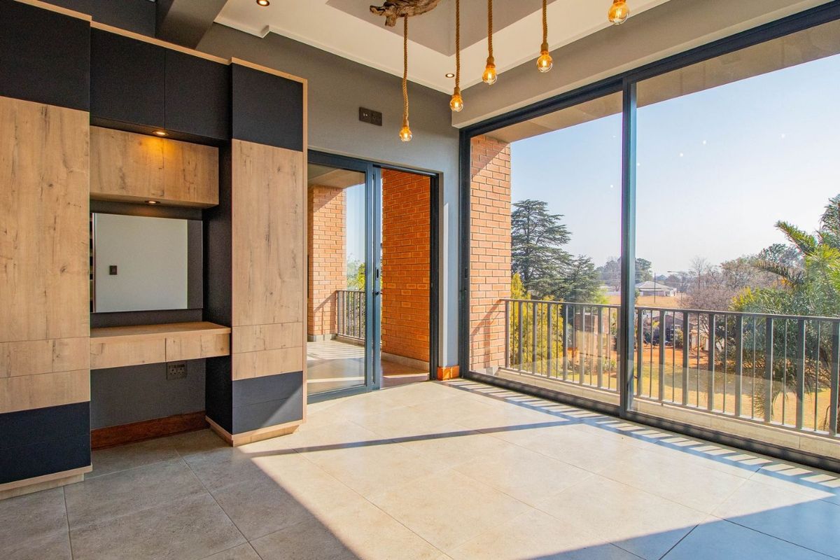 Modern bedroom featuring built-in cabinetry, large sliding glass doors leading to a balcony, and contemporary pendant lighting with neutral tiled flooring.