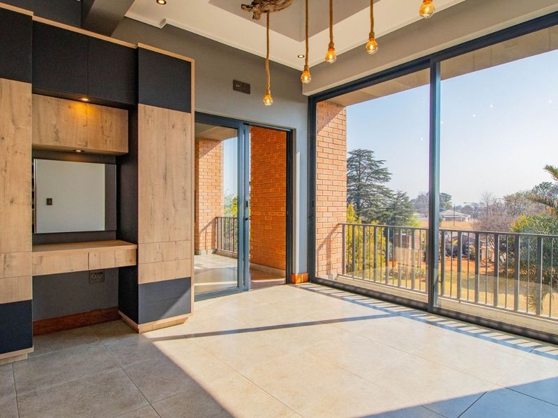 Modern bedroom featuring built-in cabinetry, large sliding glass doors leading to a balcony, and contemporary pendant lighting with neutral tiled flooring.
