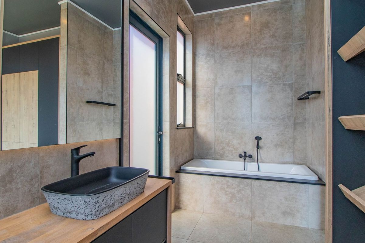 Modern bathroom featuring a vessel sink on a wooden vanity, a built-in bathtub with black fixtures, and neutral floor-to-ceiling tiling.