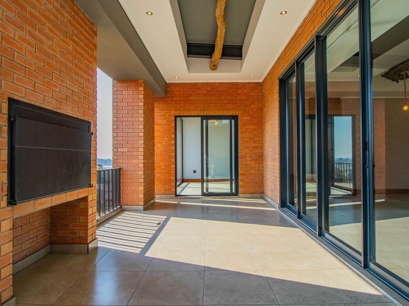 Spacious covered balcony featuring exposed brickwork, a built-in braai, tiled flooring, and large sliding glass doors providing seamless indoor-outdoor flow.