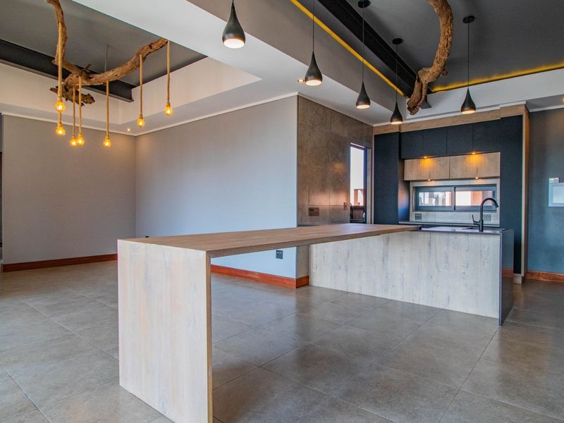 Modern open-plan kitchen and living area featuring sleek cabinetry, a large wooden island, tiled floors, and contemporary pendant lighting in a penthouse setting.