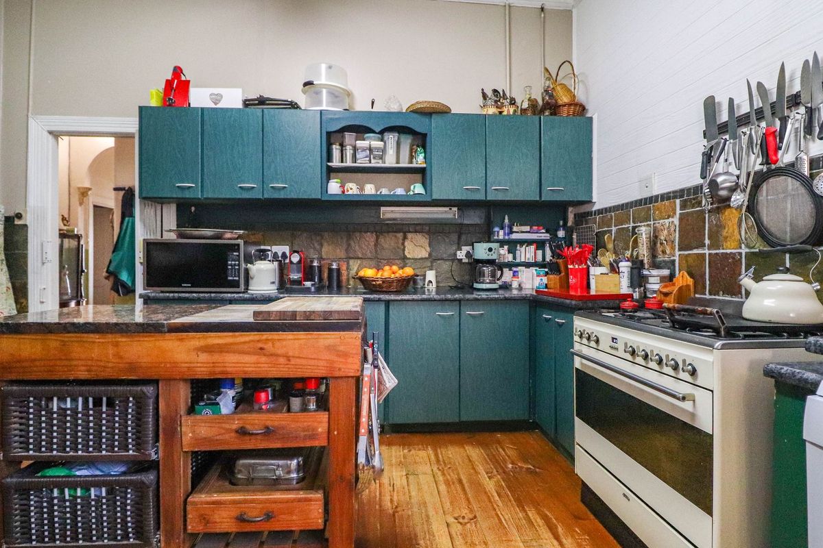 A functional kitchen featuring dark green cabinetry, a stone-tiled splashback, a freestanding gas stove, and a central timber island unit with storage.
