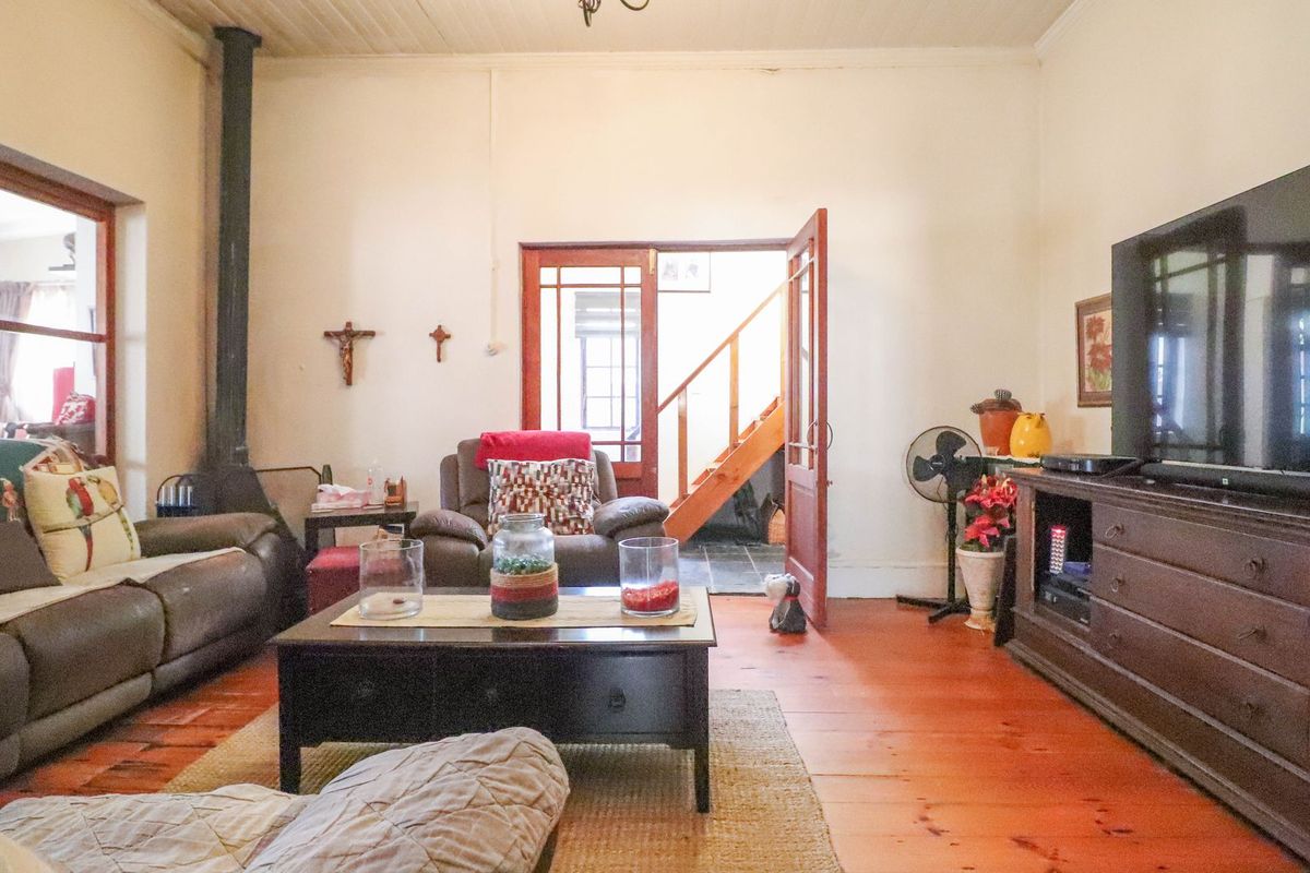 A living room featuring original timber flooring, a built-in wood-burning fireplace, and access to an internal staircase through a wooden door frame.