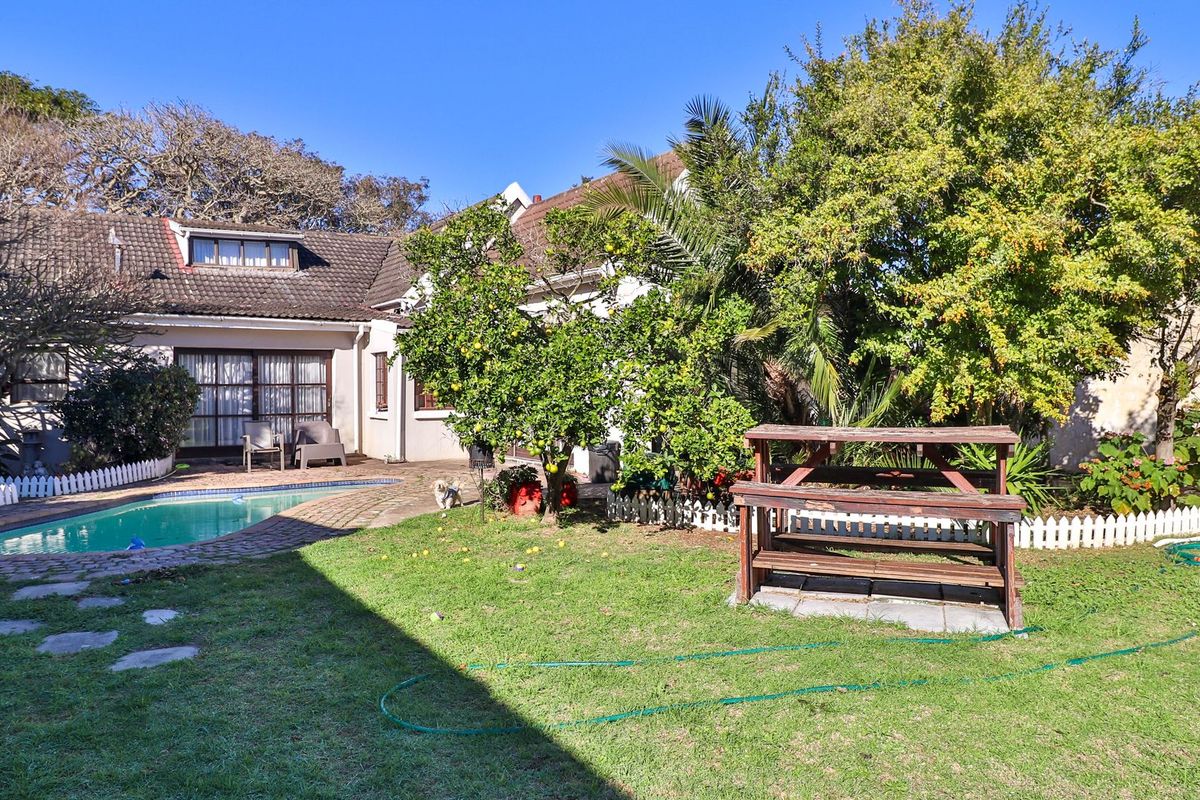Rear garden featuring a swimming pool, paved patio area, and established trees, providing a private outdoor space for relaxation and recreation.