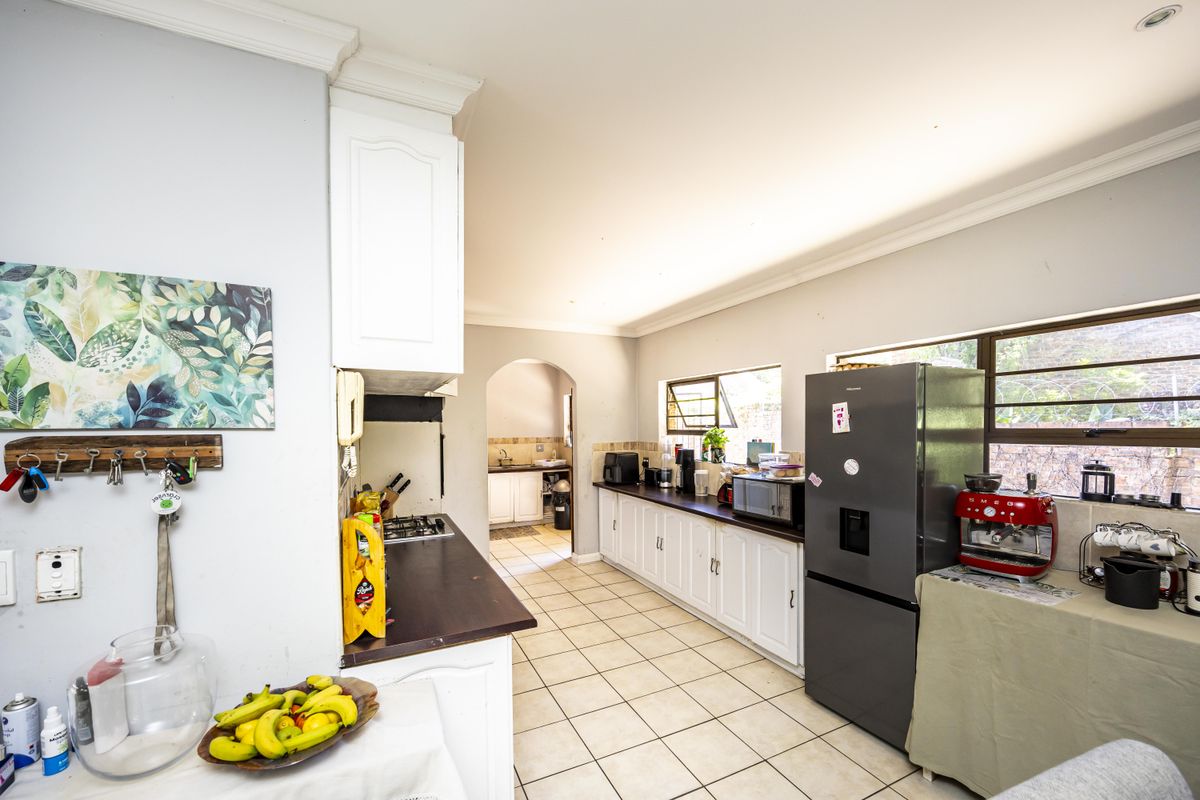 A functional kitchen featuring white cabinetry, dark countertops, tiled flooring, and an arched doorway leading to a secondary prep or scullery area.