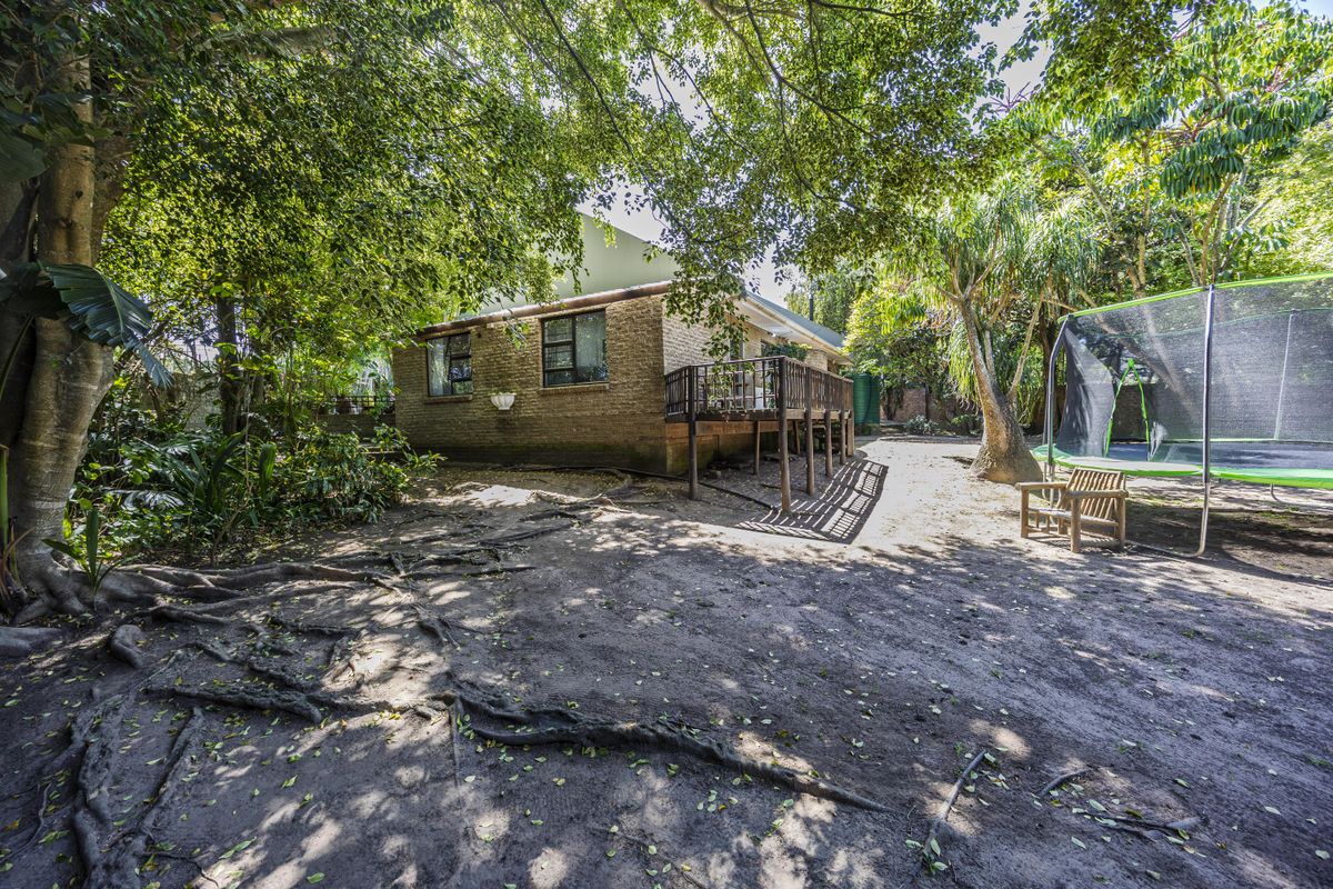 A view of the rear exterior of the house featuring a raised wooden deck, mature trees, and a spacious garden area.