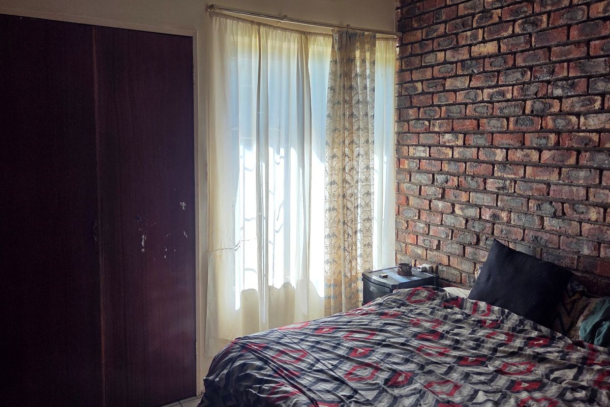 Bedroom featuring an exposed brick feature wall and a built-in wardrobe, offering a rustic aesthetic with potential for modern updates.