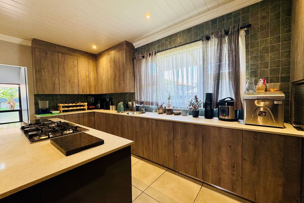 A well-appointed kitchen featuring wood-grain cabinetry, a central island with a built-in gas hob, stone countertops, and tiled splashbacks.