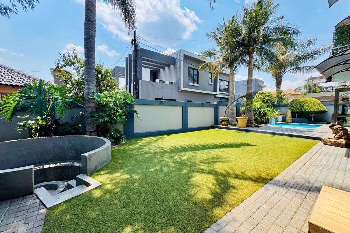 A well-maintained rear garden featuring a manicured lawn, paved pathways, a built-in concrete seating area, and a swimming pool in the background.