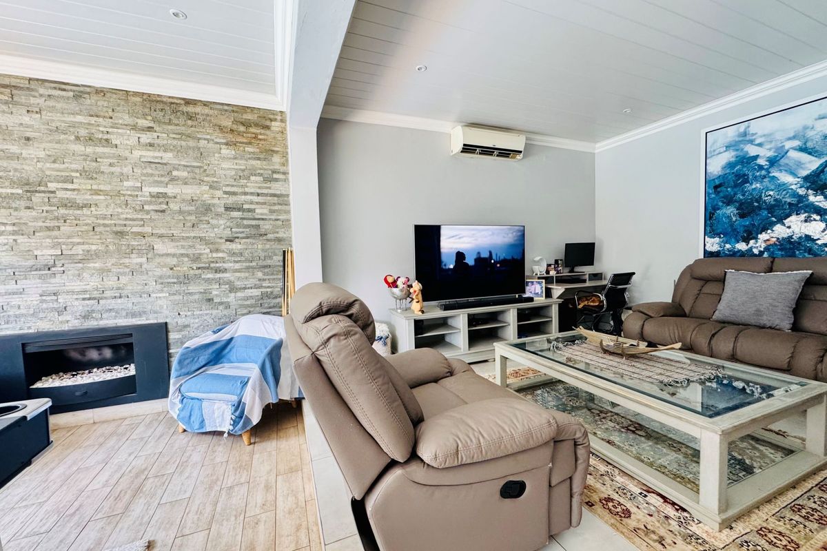 Spacious living room featuring a stone-clad fireplace, wood-look tile flooring, and a split-system air conditioning unit.