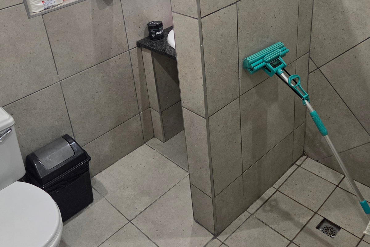 A functional bathroom featuring neutral ceramic tiling, a toilet, and a partitioned shower area with a built-in wall niche.