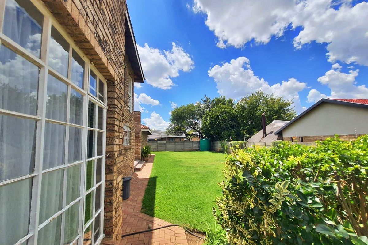 A view of the rear garden featuring a brick-paved walkway, well-maintained lawn, and perimeter walling.