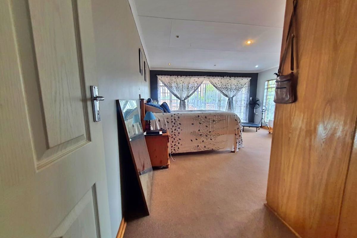 A spacious bedroom featuring neutral wall tones, carpeted flooring, and large windows with security bars, providing ample natural light.
