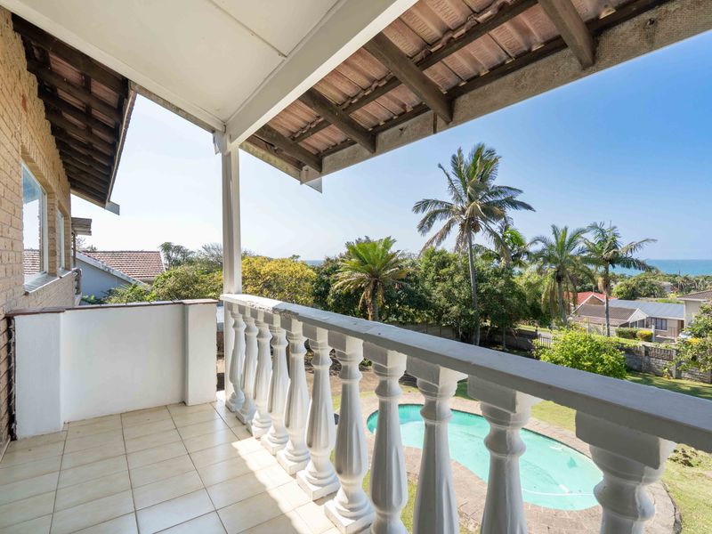 Covered balcony featuring a classic balustrade, tiled flooring, and exposed timber rafters, offering elevated views over the garden and swimming pool.