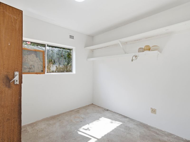 A small, empty utility space featuring white walls, built-in shelving, and an unfinished concrete floor, suitable for storage or a workshop area.