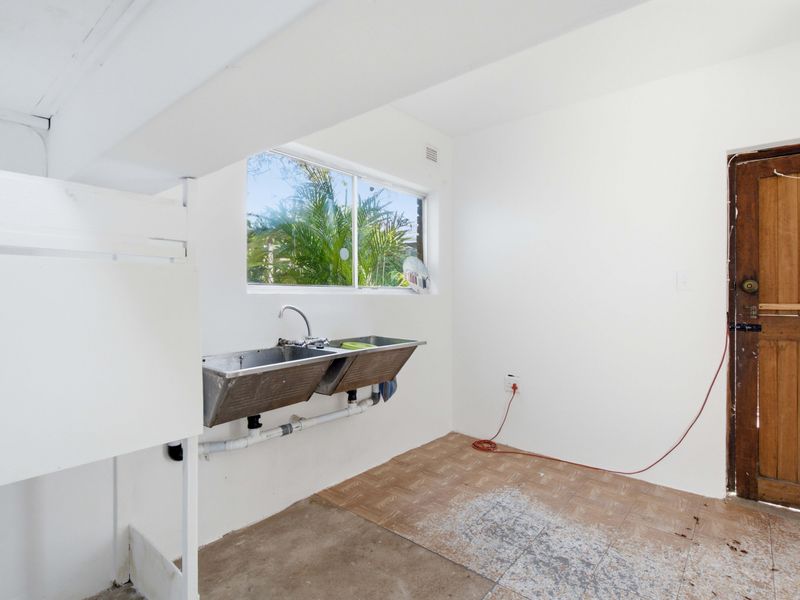A functional laundry area featuring a double stainless steel sink, exposed plumbing, and direct access to the exterior via a timber door.