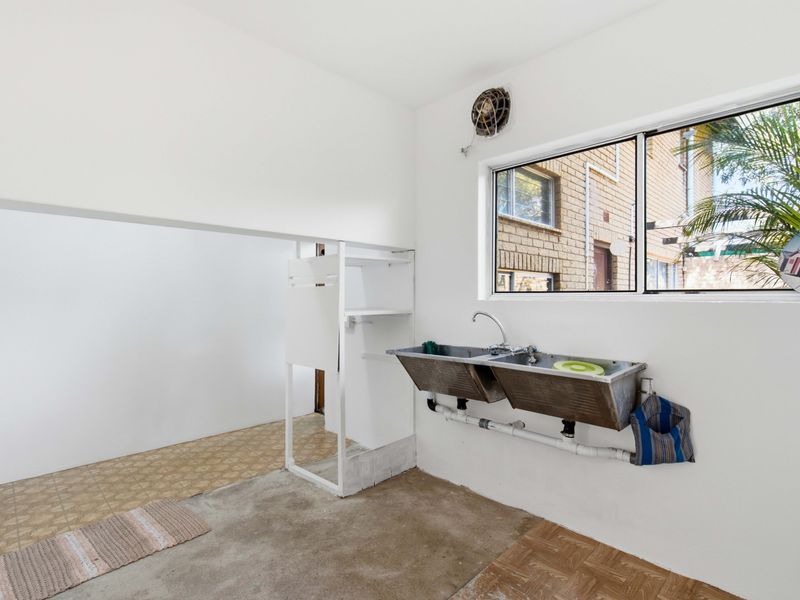 A functional laundry area featuring a double stainless steel sink, wall-mounted extractor fan, and built-in shelving, offering a practical space for utility tasks.