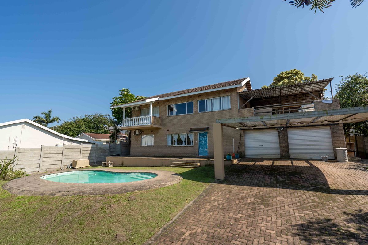 Rear view of a double-story brick house featuring a swimming pool, paved driveway, double garage, and an upper-level balcony.