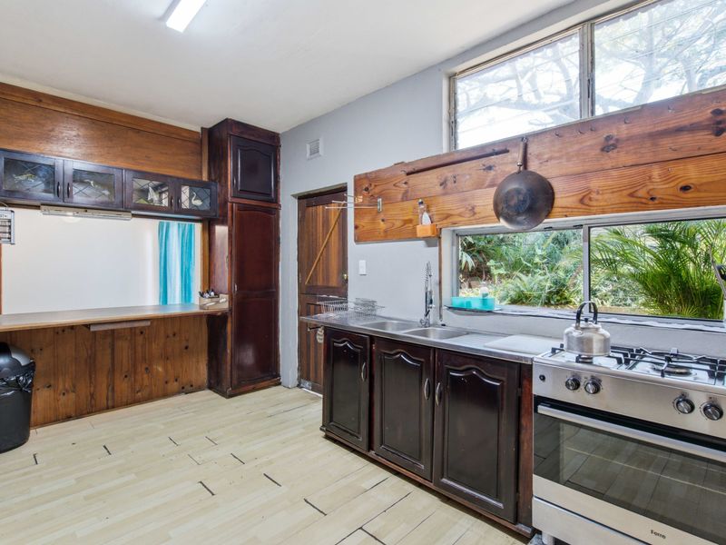 A functional kitchen featuring dark wood cabinetry, a stainless steel gas stove, and large windows providing natural light and garden views.