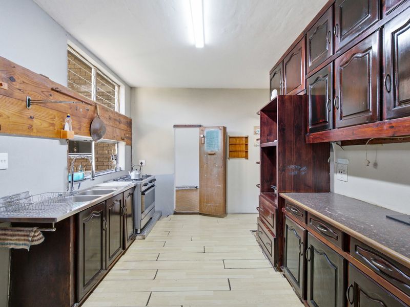 A functional kitchen featuring dark wood cabinetry, laminate countertops, a stainless steel double sink, and a freestanding stove with tiled flooring.