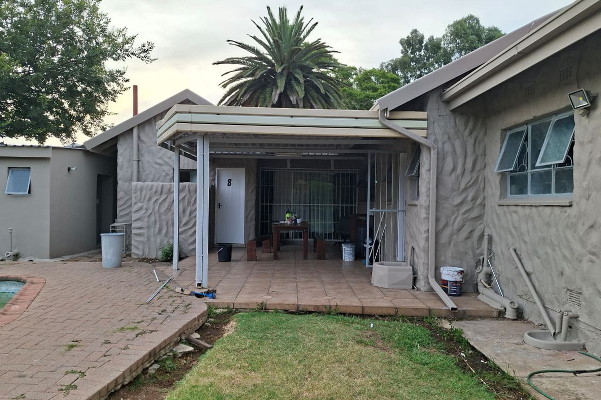 Rear view of the property featuring a covered patio area, paved pool surround, and textured exterior wall finish.
