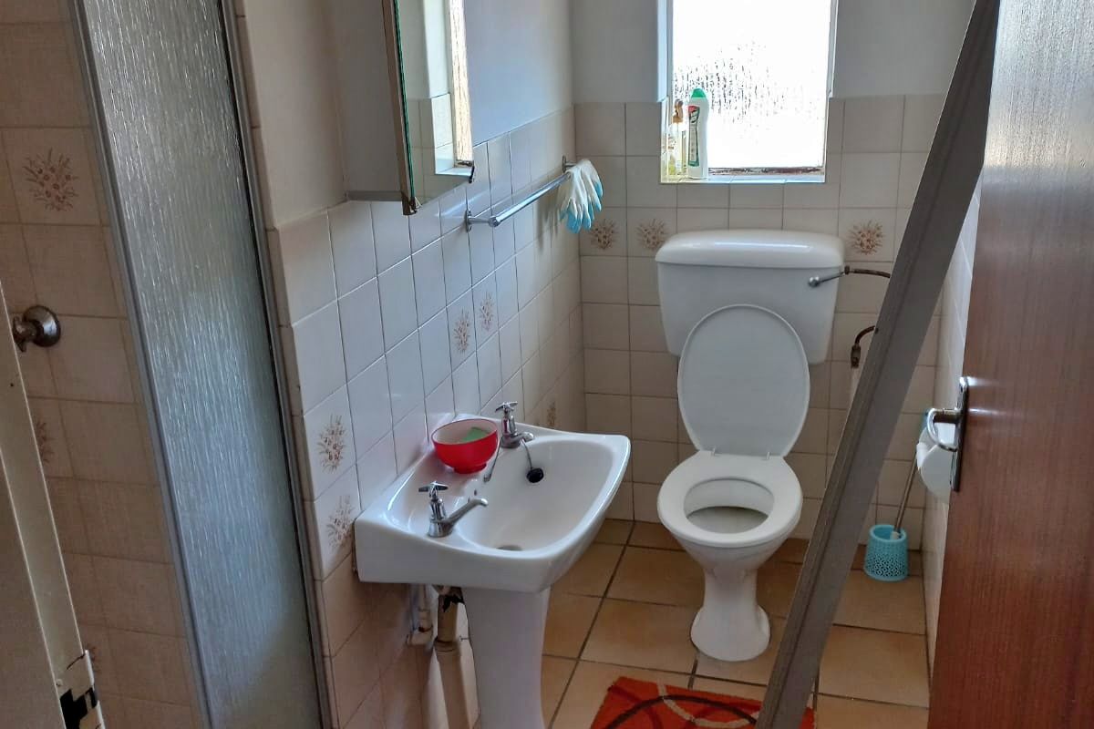 A compact bathroom featuring a pedestal basin, toilet, and a shower enclosure with tiled walls and flooring.