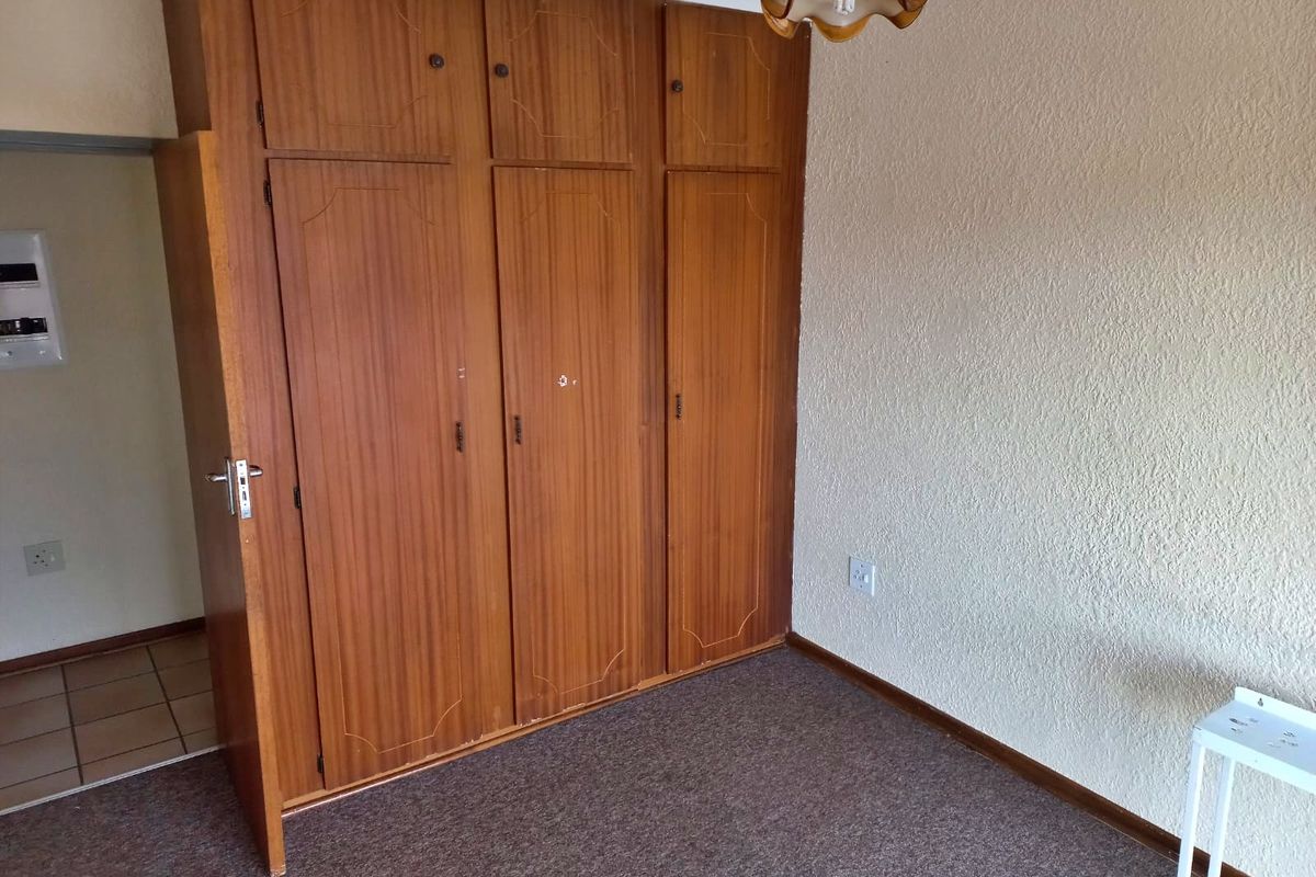 A bedroom featuring built-in wooden cupboards, textured wall finishes, and carpeted flooring.