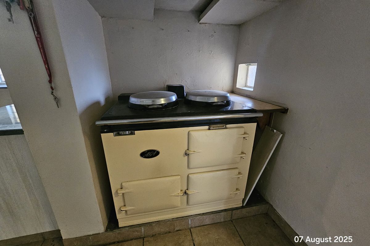 A classic cream-colored AGA range cooker set within a recessed kitchen alcove, featuring tiled flooring and a small side window.