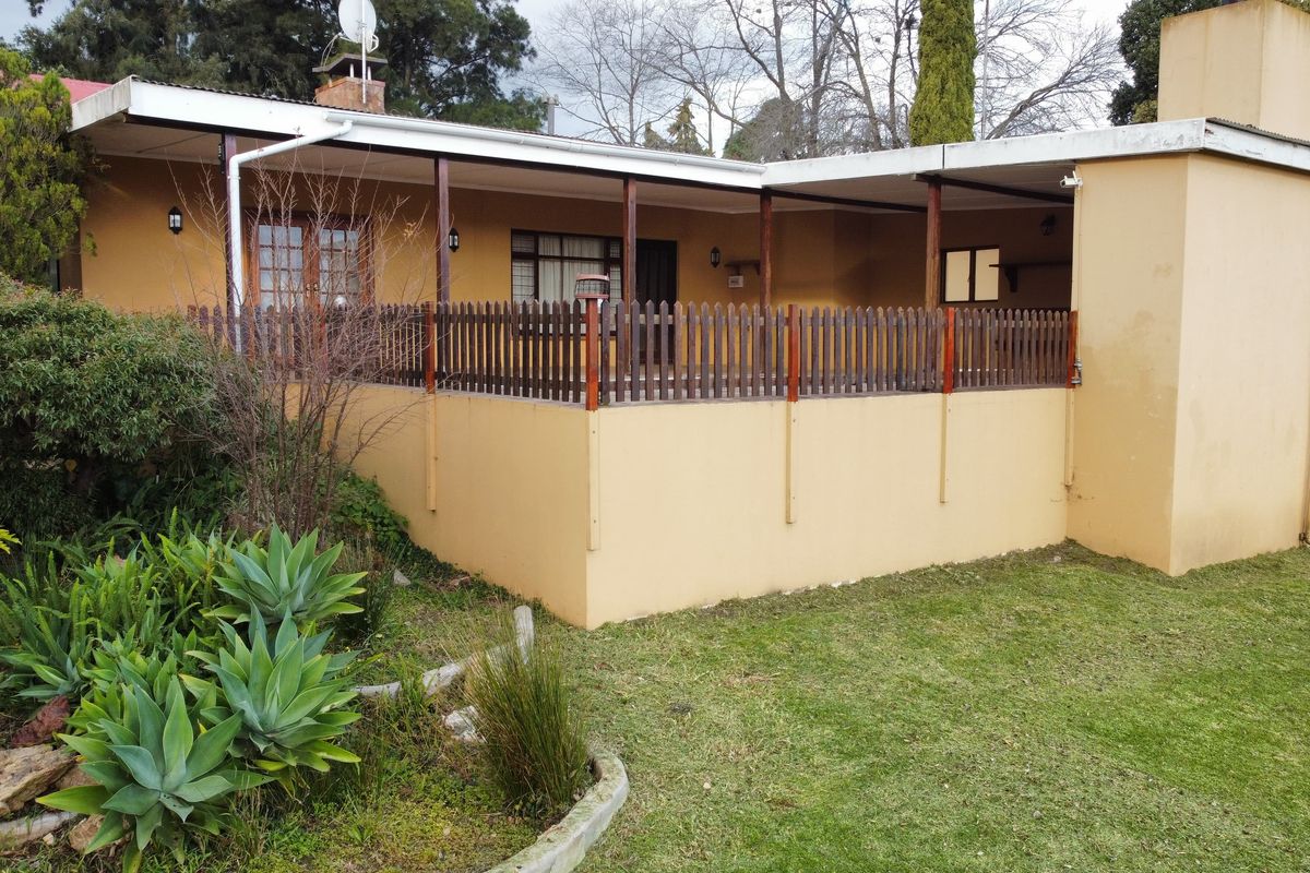A view of the rear exterior of the farm property, featuring a covered patio area with a wooden fence and surrounding garden.