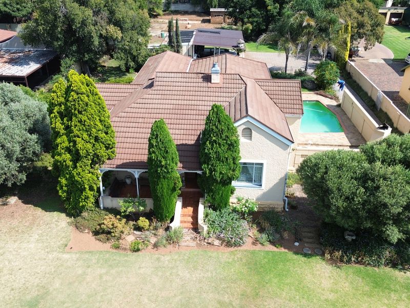 Aerial view of a residential property featuring a tiled roof house, a swimming pool, and established garden landscaping.