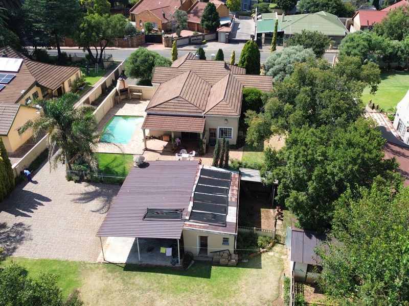 Aerial view of the property featuring a swimming pool, covered patio with built-in braai, paved driveway, and solar panel installations on the roof.