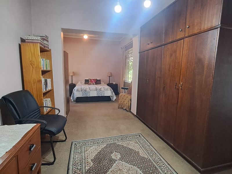 Spacious bedroom featuring extensive built-in wooden cabinetry and carpeted flooring, offering a functional layout with an adjoining sleeping area.