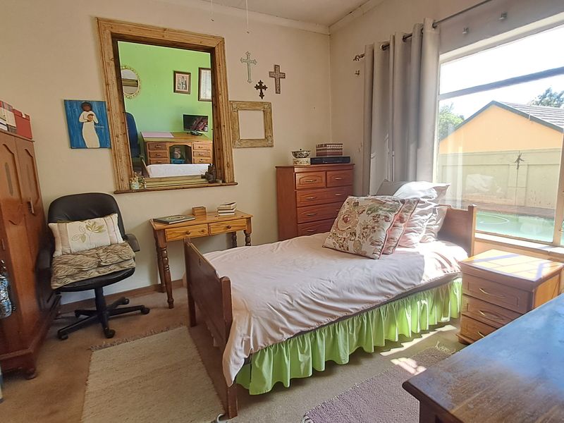 A bedroom featuring a large window with security bars, carpeted flooring, and neutral wall finishes, offering a view of the outdoor pool area.