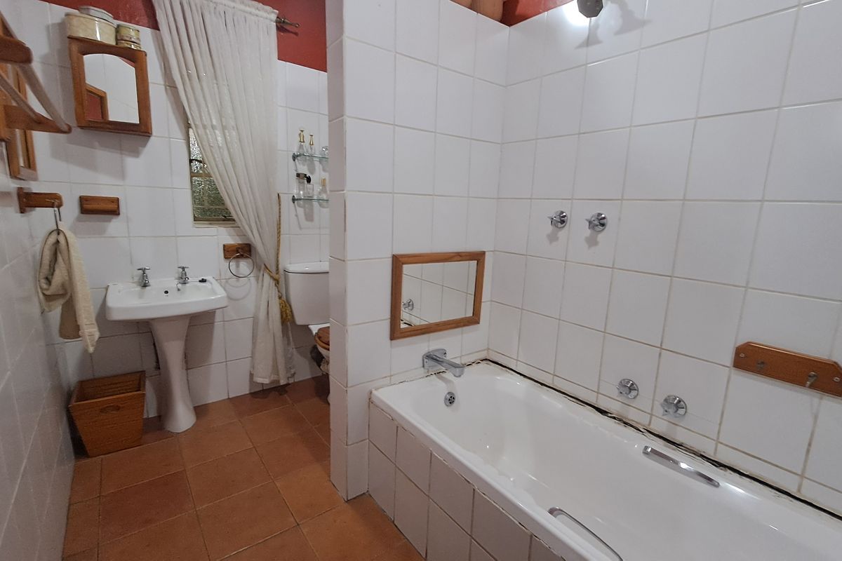 A dated bathroom featuring a pedestal basin, built-in bathtub, and ceramic tiling throughout. The space requires cosmetic updates to improve its overall condition.
